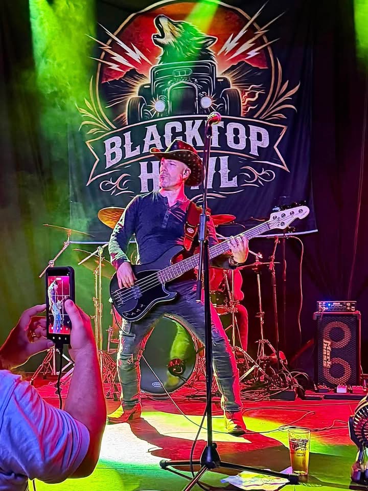 Blacktop Howl bassist under stage lights in front of the band banner